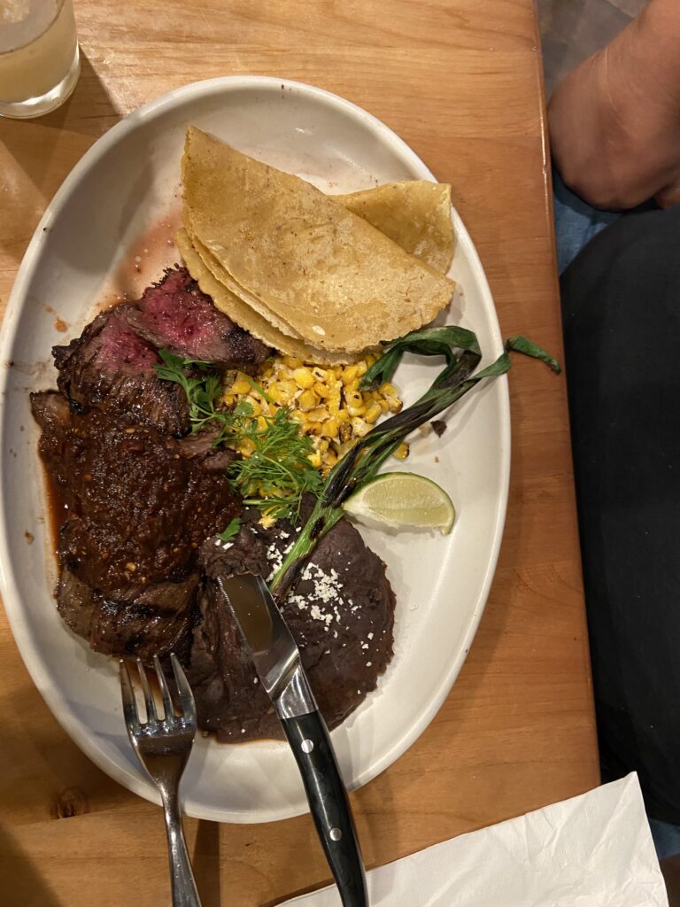Carne Asada skirt steak, spicy ancho Chile salsa, Chile-lime corn, refried black beans, queso blanco (white cheese, aka fresh , soft cheese), grilled knob onion, and two housemate corn tortillas.