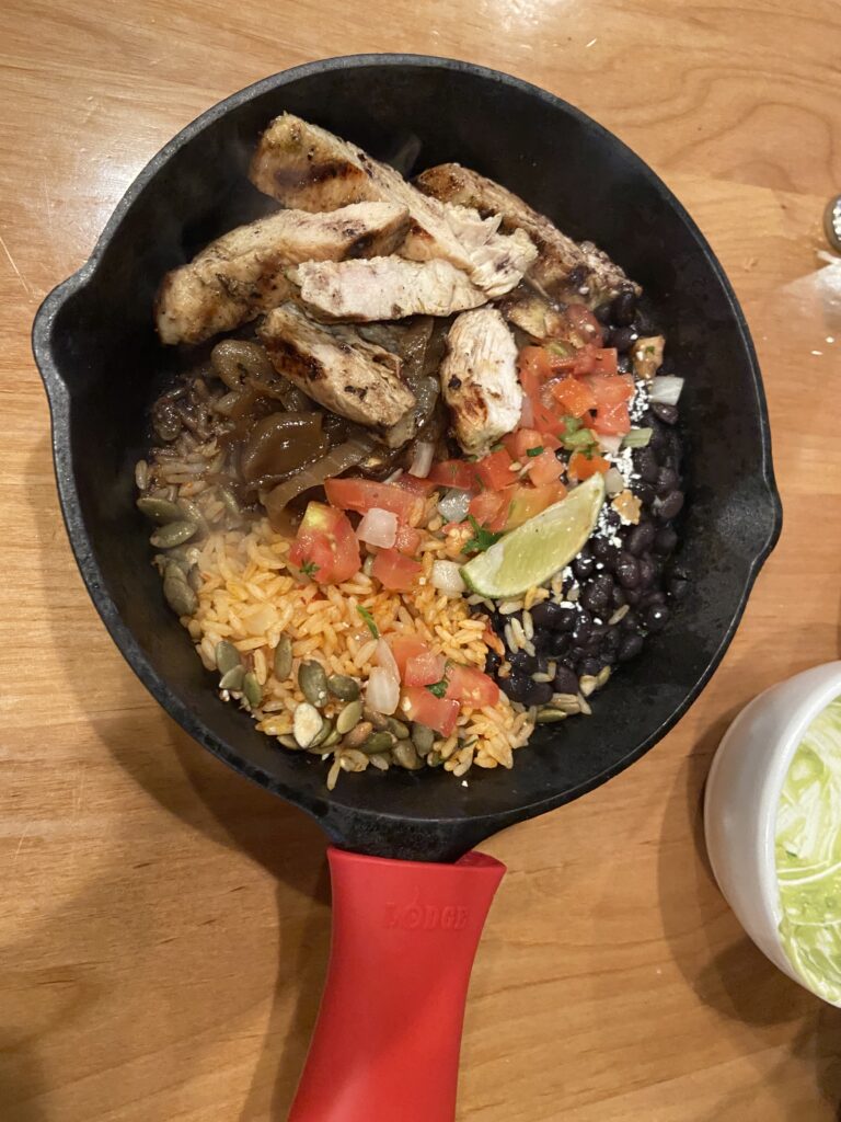 Fajitas with grilled chicken, grilled onions, Mexican rice, black beans, and pico de gallo in a black iron skillet.