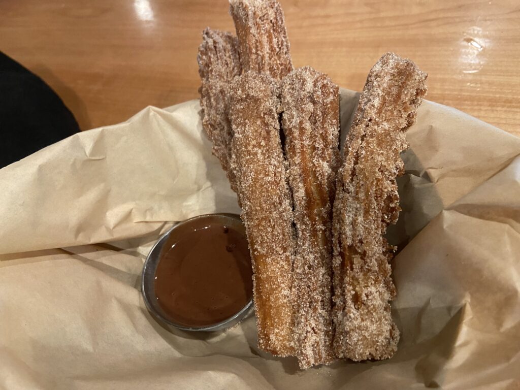 5 Churros coated in cinnamon sugar with chocolate sauce on the side.