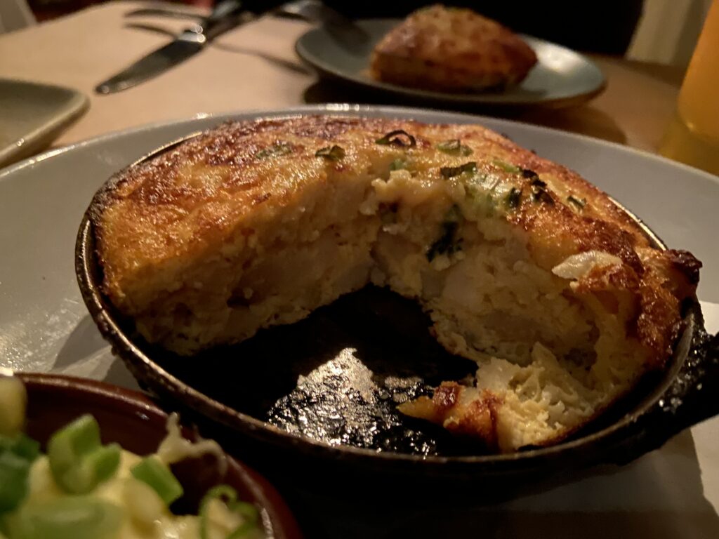 Tortilla Espanola cross cut. A baked egg and potato dish with green onion on top. A third piece was taken out to show the middle.
