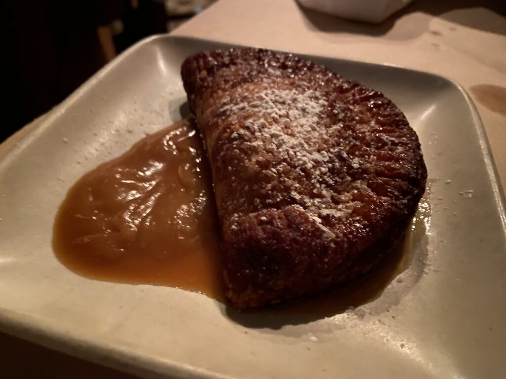 Apple Empanada with apple glaze on the side and powder sugar on top.