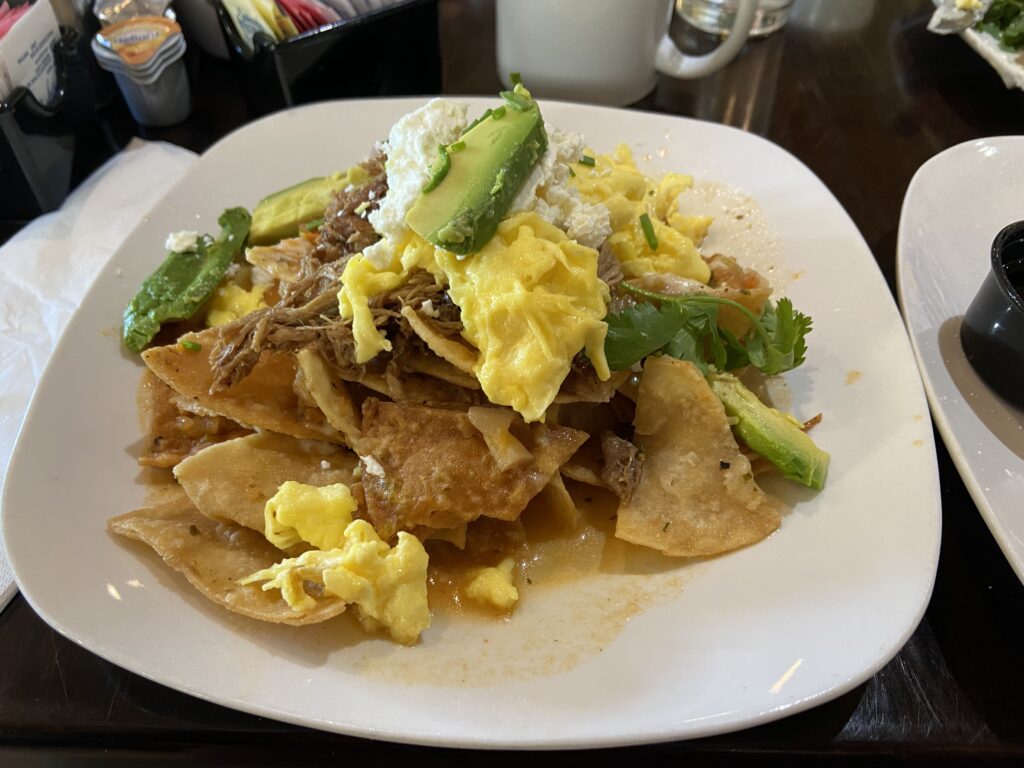 Tortilla chips smothered with green chilaquiles sauce, shredded pork, scrambled eggs, avocado slices, Mexican cheese, and cilantro.
