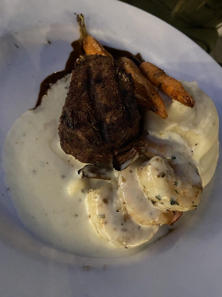 Steak with mashed potatoes, 3 shrimps, and 3 carrots carrots in a white cream sauce.
