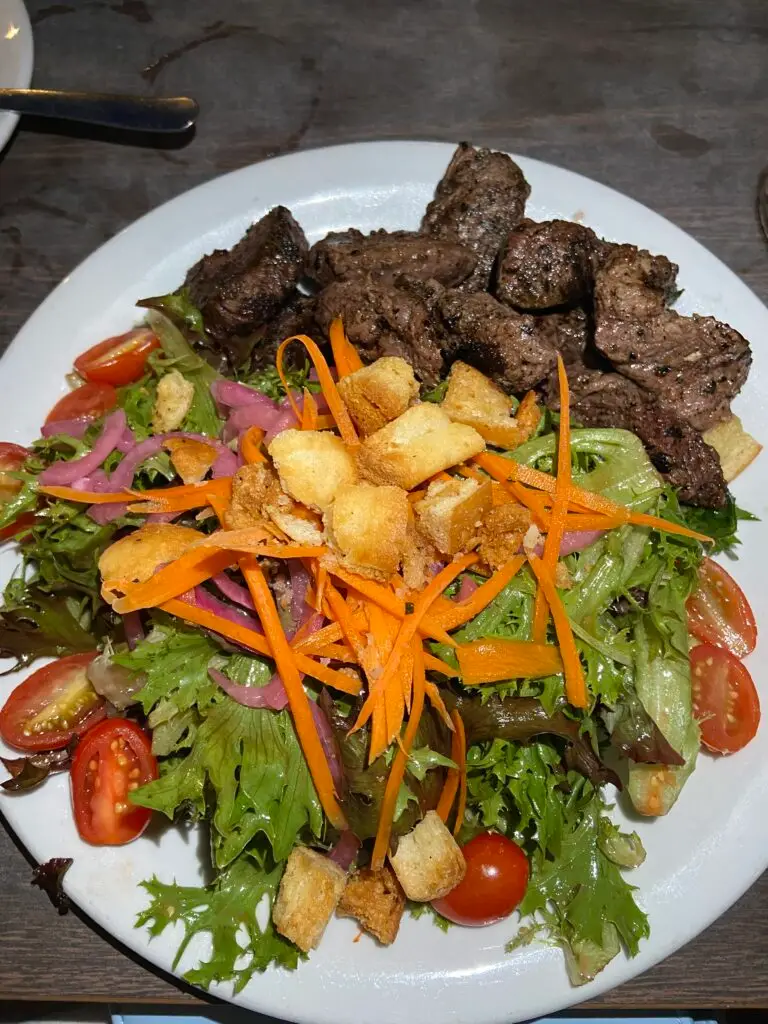 Salad with tomatoes, red onion, carrot, croutons, and steak.