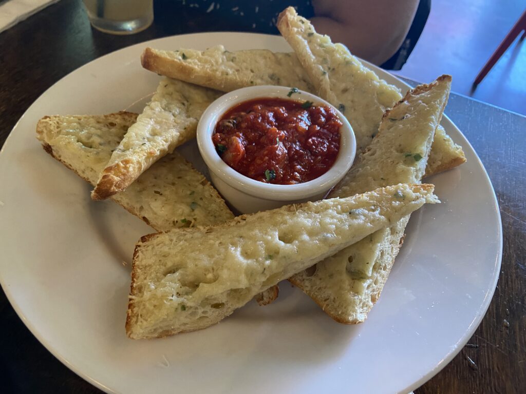 Six triangular shaped Parmesan Bread. In the middle is a small ramekin with marinara sauce.