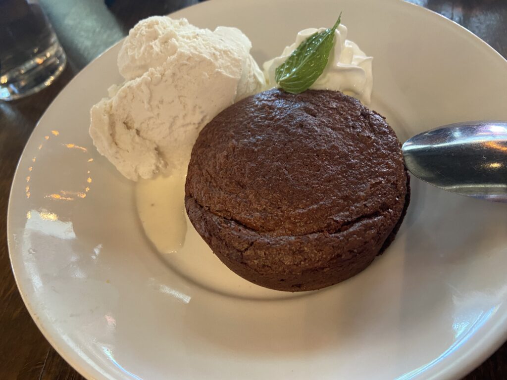 A spherical chocolate ball with two scoops of vanilla ice cream and a sprig of mint on top.