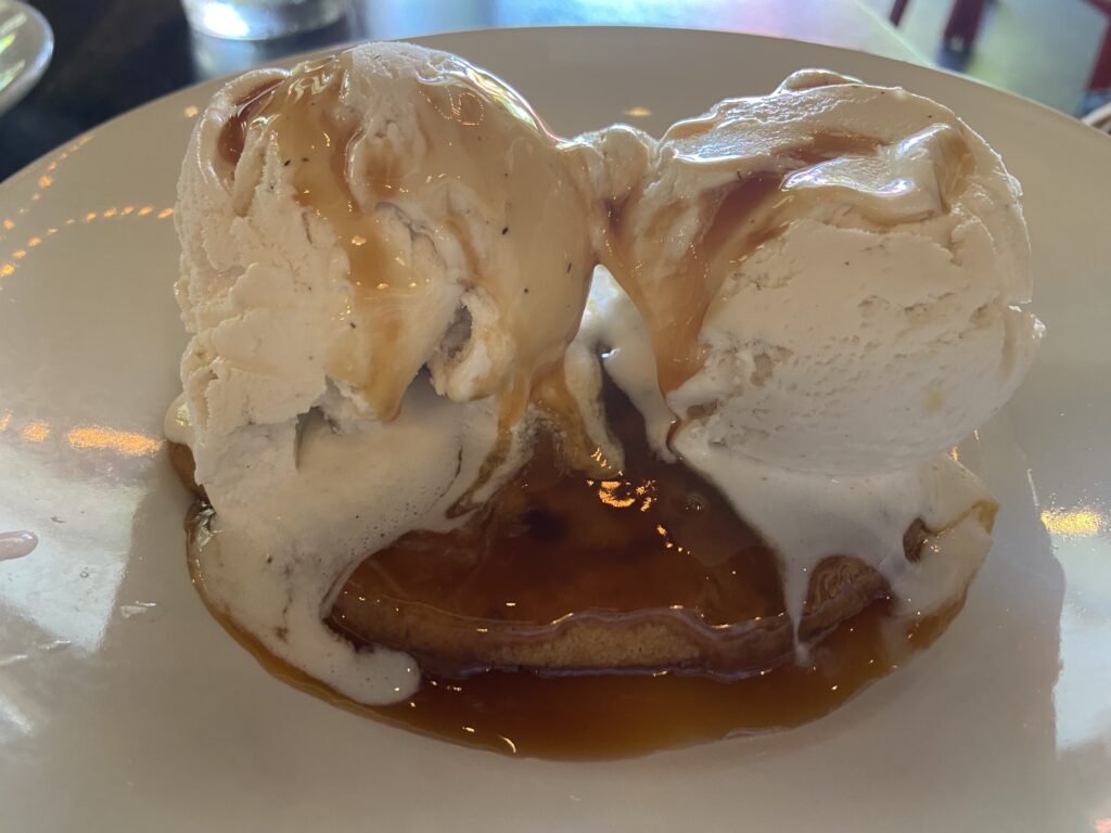 two vanilla gelato scoops on top of a chocolate chip cookie all drenched with caramel.  
