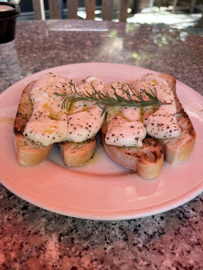 Fresh mozzarella cheese with cracked pepper and olive oil on a bed of four slices of toasted baguette and topped with fresh thyme.