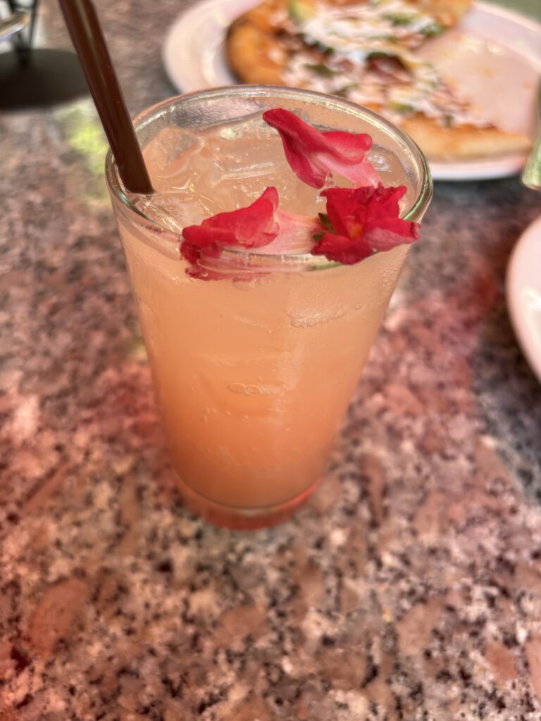 A non-alcoholic drink with guava, lemon, simple syrup, and elder tonic topped with flower peddles.